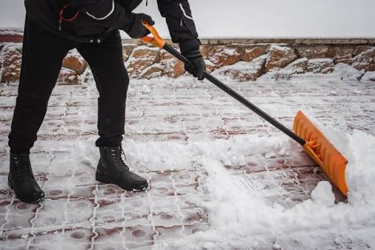 Mitarbeiter räumt frühmorgens Schnee vor einem Gebäudeeingang